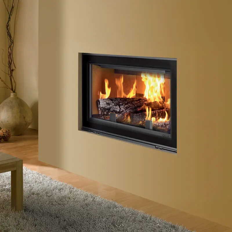 Cheminée à Bois Moderne Encastrée pour un Salon Design Cheminée à bois moderne encastrée dans un mur beige avec flammes vives, tapis gris et vase décoratif.