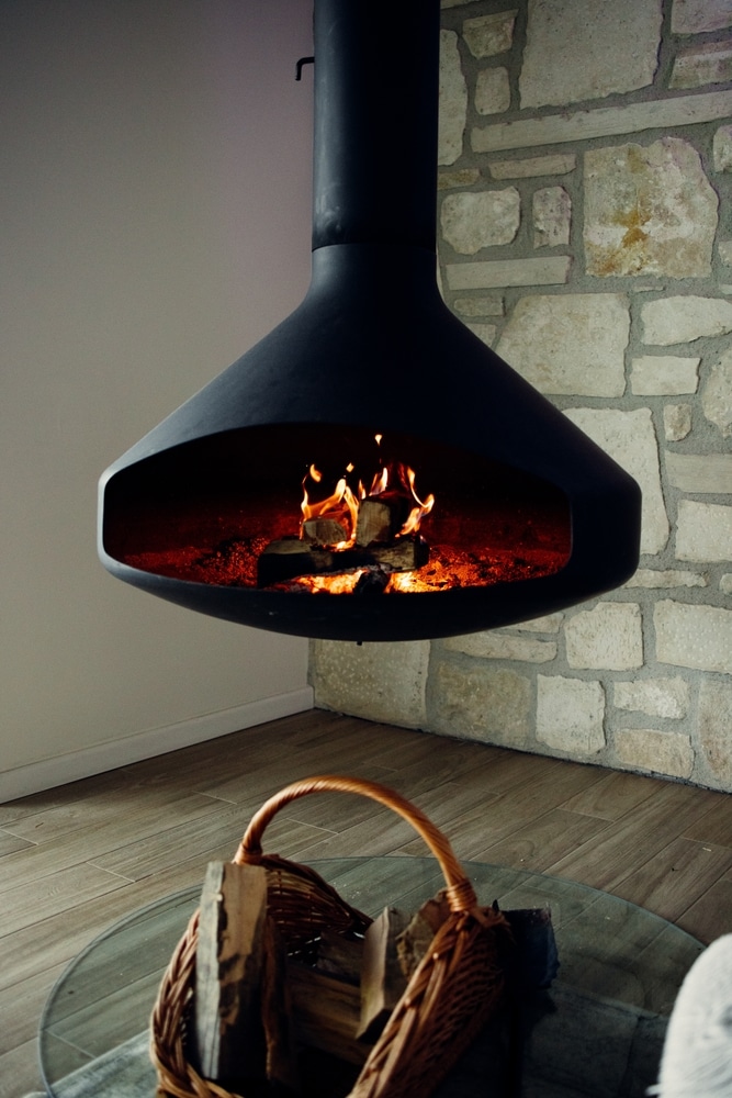 Cheminée suspendue noire design pour intérieur chaleureux Cheminée suspendue noire avec feu de bois crépitant devant un mur en pierre, ambiance chaleureuse et moderne.