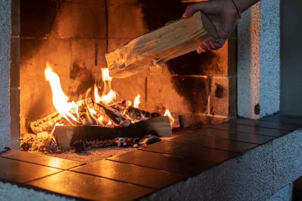 Feu de cheminée : ajout d'une bûche de bois pour la chaleur Main ajoutant une bûche de bois dans une cheminée allumée aux flammes chaleureuses et crépitantes.