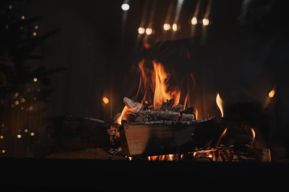 Feu de Cheminée Chaleureux et Ambiance Hivernale Cocooning Bûches de bois brûlant dans une cheminée chaleureuse avec une ambiance de fête tamisée en arrière-plan.