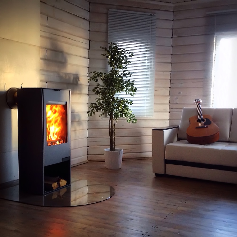 Poêle à bois et ambiance cocooning dans un salon en bois Salon de chalet chaleureux avec un poêle à bois allumé, une plante verte et une guitare sur un canapé blanc.