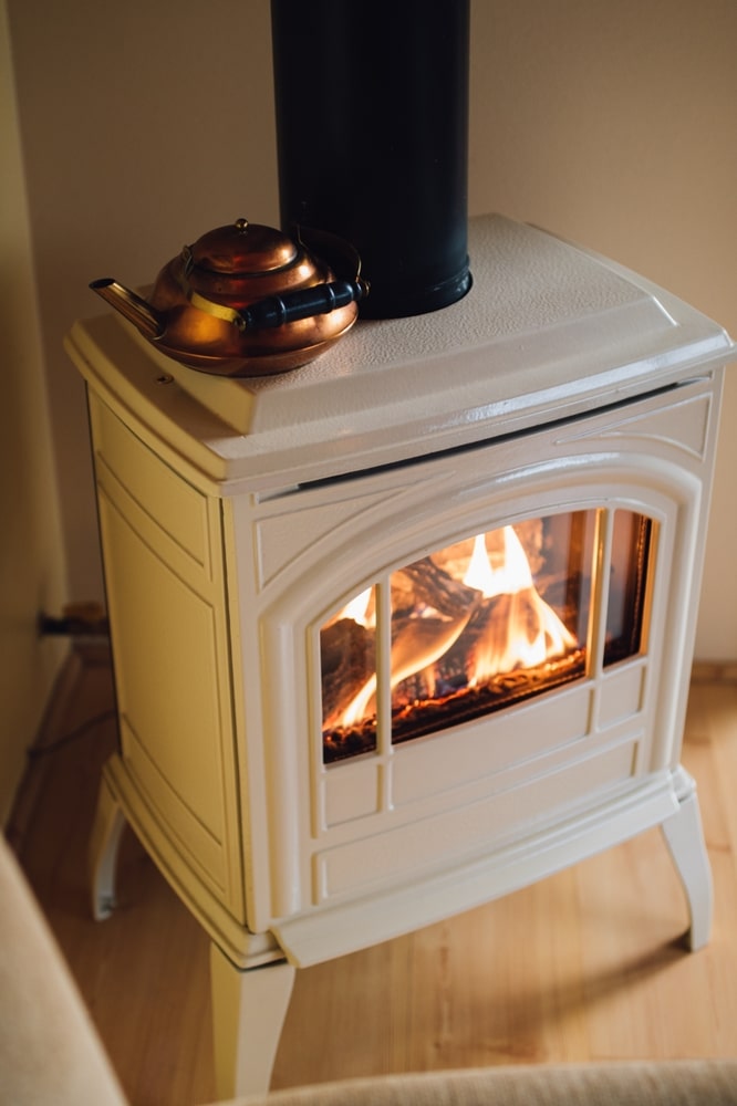 Poêle Blanc Design avec Feu de Cheminée et Théière Cuivre Poêle blanc élégant avec feu de bois visible et théière en cuivre rétro, créant une ambiance chaleureuse.