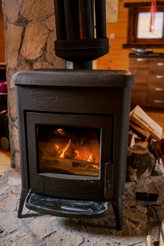 Poêle à Bois en Fonte : Feu et Ambiance de Chalet Poêle à bois en fonte noir allumé devant un mur de pierre dans un chalet à l'ambiance chaleureuse.