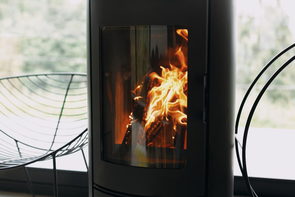 Poêle à Bois Design Noir : Ambiance Chaleureuse de Salon Poêle à bois moderne avec feu crépitant, chaise design et vue sur jardin. Ambiance chaleureuse et design épuré.